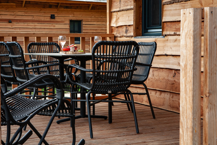 Terraza al aire libre con sillas negras y mesa en Heydehuis glamping, rodeada de paredes de madera.