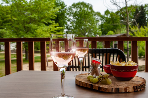 Twee glazen rosé, chips en druiven op tafel buiten bij glampingaccommodatie Heydehuis, omgeven door natuur.