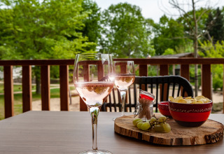 Dos copas de vino rosado, patatas fritas y uvas en una mesa exterior en el alojamiento glamping Heydehuis.