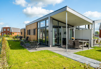 Moderne tiny house ved Tusken de Marren i Holland med store vinduer, terrasse og grøn have under blå himmel.