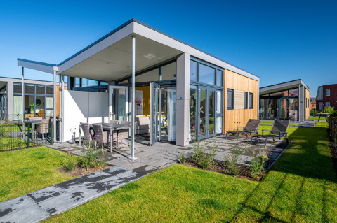 Modern tiny house Knilles at Tusken de Marren in the Netherlands, with patio, chairs, and green lawn.