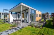 Modern tiny house Knilles at Tusken de Marren in the Netherlands, with patio, chairs, and green lawn.