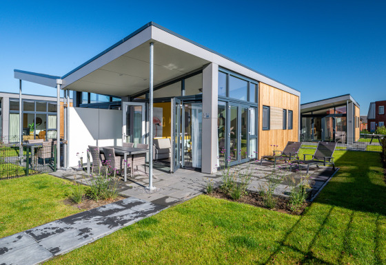 Modern tiny house Knilles at Tusken de Marren in the Netherlands, with patio, chairs, and green lawn.