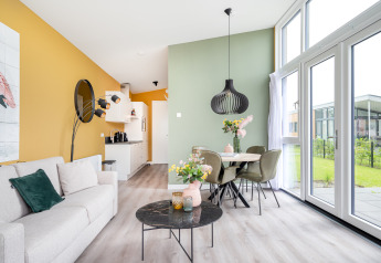 Moderne woon- en eetruimte in Tiny House Knilles met grote ramen, pastelkleuren en stijlvolle decoratie.