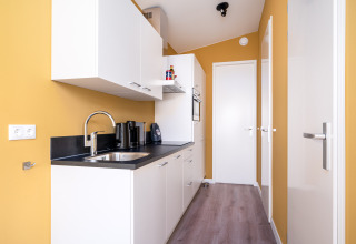 Modern small kitchen in Knilles tiny house at Tusken de Marren, Netherlands, with yellow walls and white cabinets
