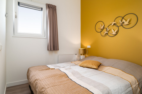 Schlafzimmer im Tiny House Knilles bei Tusken de Marren, Niederlande, mit gelber Wand und gemütlichem Bett.
