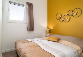 Dormitorio en la tiny house Knilles en Tusken de Marren, Países Bajos, con pared amarilla y cama cómoda.