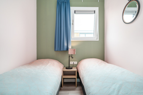 Bright bedroom in Knilles tiny house at Tusken de Marren, Netherlands, with two single beds and a window.
