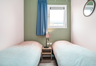 Bright bedroom in Knilles tiny house at Tusken de Marren, Netherlands, with two single beds and a window.