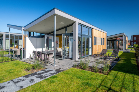 Modern tiny house 'Knilles' with glass walls and patio at Tusken de Marren holiday park, Netherlands.