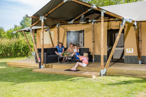 Gezin ontspant op de veranda van Stuuflodge safaritent in Kampeerdorp de Zandstuve, Nederland.