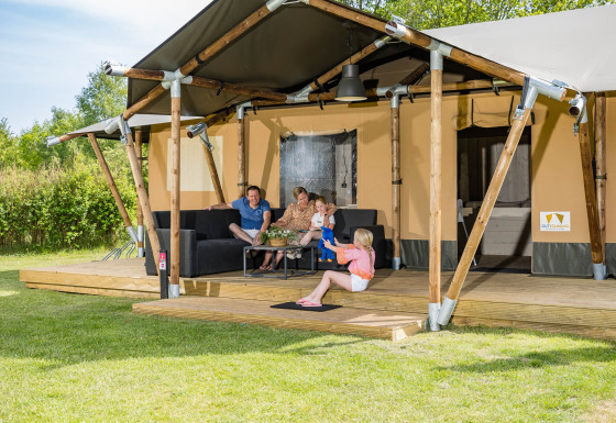 Familia relajándose frente a la tienda safari Stuuflodge en Kampeerdorp de Zandstuve, Países Bajos.