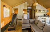 Binnenzicht van een Stuuflodge safaritent met een zetel, glijbaan en keuken bij Kampeerdorp de Zandstuve.