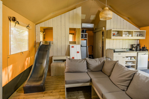 Vista interior de una tienda safari Stuuflodge con sofá, tobogán y cocina en Kampeerdorp de Zandstuve.