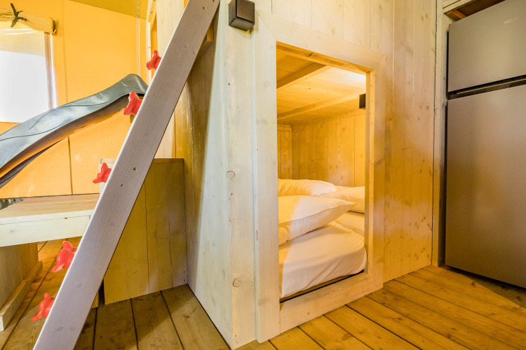 Vista interior de una tienda safari Stuuflodge en Kampeerdorp de Zandstuve con paredes y cama de madera.