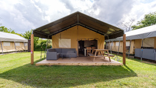 Stuuflodge Bella safaritent met houten veranda, loungeset en picknicktafel bij Kampeerdorp de Zandstuve, Nederland.