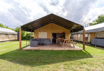 Stuuflodge Bella Safarizelt mit Holzterrasse, Sitzmöglichkeiten und Picknickbank in Kampeerdorp de Zandstuve, Niederlande.