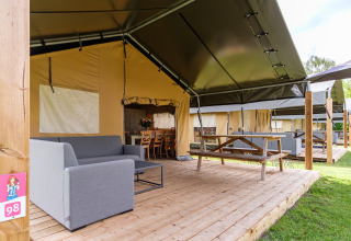 Tienda safari Stuuflodge Bella con terraza de madera, sofá y mesa de picnic en Kampeerdorp de Zandstuve.