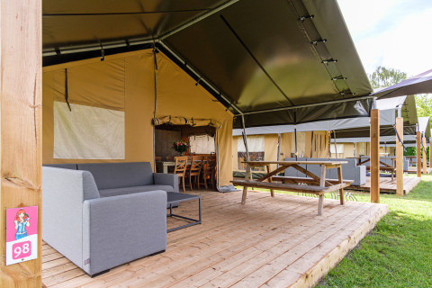 Tienda safari Stuuflodge Bella con terraza de madera, sofá y mesa de picnic en Kampeerdorp de Zandstuve.