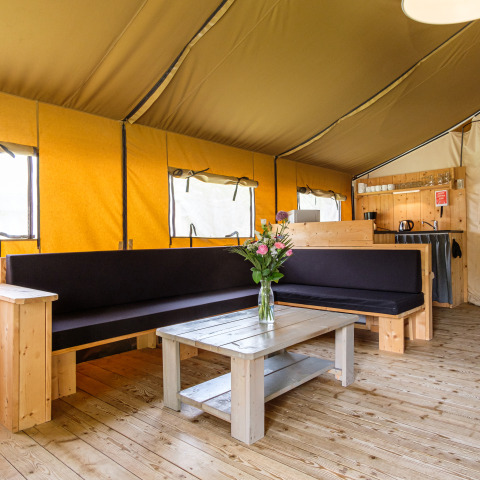 Innenaufnahme des Stuuflodge Bella Safari-Zelts mit Holzmöbeln und Blumenstrauß auf dem Tisch.
