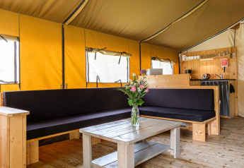 Innenaufnahme des Stuuflodge Bella Safari-Zelts mit Holzmöbeln und Blumenstrauß auf dem Tisch.