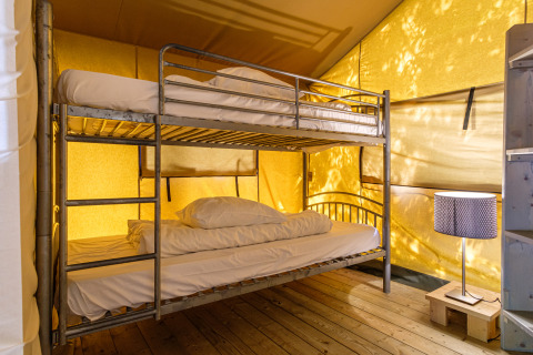 Interior de una tienda safari en Kampeerdorp de Zandstuve con litera, lámpara y suelo de madera.