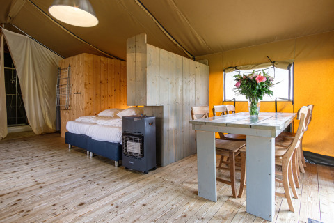 Vista interior de la tienda safari Stuuflodge Bella con cama y mesa en Kampeerdorp de Zandstuve, Países Bajos.