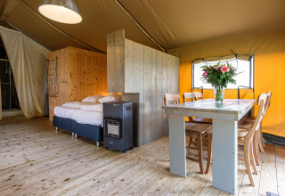 Vista interior de la tienda safari Stuuflodge Bella con cama y mesa en Kampeerdorp de Zandstuve, Países Bajos.