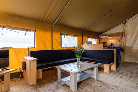 Vista interior de Stuuflodge Bella, una tienda safari con muebles de madera y sala cómoda en Holanda.