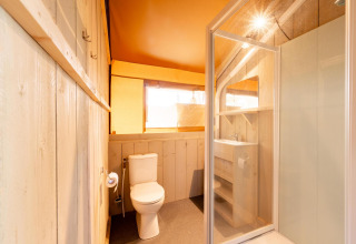 Bagno all'interno di una tenda safari Villatent Nomad con wc, lavabo, doccia e dettagli in legno.