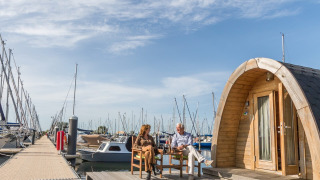 Pareja relajándose frente a la tiny house Water bubbles en Marina Parcs Almere, Países Bajos, rodeados de barcos.