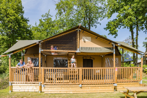 Familia disfruta de un día soleado en la terraza de una tienda safari Stuuflodge DeLuxe en Kampeerdorp de Zandstuve.