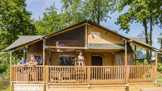 Familie nyder en solrig dag på terrassen af en Stuuflodge DeLuxe safari-telt i Kampeerdorp de Zandstuve.