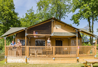Familie nyder en solrig dag på terrassen af en Stuuflodge DeLuxe safari-telt i Kampeerdorp de Zandstuve.