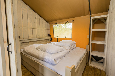 Camera da letto della Stuuflodge DeLuxe, tenda safari con letto e scaffale in legno nei Paesi Bassi.