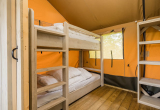 Interieur van een safaritent met stapelbedden en houten vloer bij Kampeerdorp de Zandstuve, Nederland.