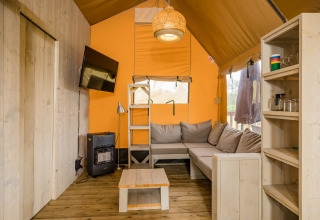 Intérieur du safari-tente Stuuflodge DeLuxe avec canapé, TV et étagères en bois à Kampeerdorp de Zandstuve, Pays-Bas.