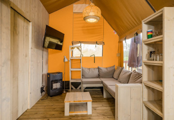 Interieur van Stuuflodge DeLuxe safaritent met zithoek, tv en houten rek bij Kampeerdorp de Zandstuve, Nederland.