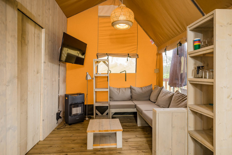 Innenraum vom Stuuflodge DeLuxe Safarizelt mit Sofa, TV und Holzregalen bei Kampeerdorp de Zandstuve, Niederlande.