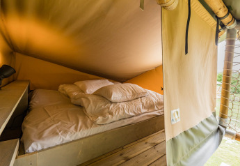 Interior view of a cozy bed in Stuuflodge DeLuxe safari tent at Kampeerdorp de Zandstuve, Netherlands.