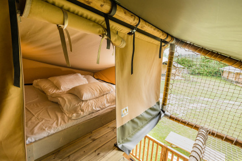 Vista interior de la tienda safari Stuuflodge DeLuxe en Kampeerdorp de Zandstuve, con cama y paisaje exterior.