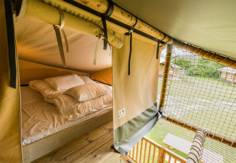 Vista interior de la tienda safari Stuuflodge DeLuxe en Kampeerdorp de Zandstuve, con cama y paisaje exterior.