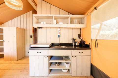 Area cucina interna nella tenda safari Villatent Nomad con pannelli in legno, mensole aperte e elettrodomestici.