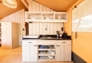 Area cucina interna nella tenda safari Villatent Nomad con pannelli in legno, mensole aperte e elettrodomestici.