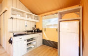 Cucina ben attrezzata con frigorifero nella tenda safari Villatent Nomad, legno chiaro e luce naturale.