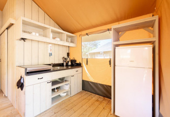 Cuisine bien équipée avec réfrigérateur dans la tente safari Villatent Nomad, bois clair et lumière naturelle.