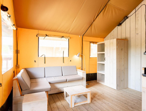 Interior de una tienda safari Villatent Nomad con muebles de madera clara, sofá gris y paredes de lona beige.