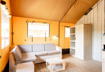 Innenraum eines Villatent Nomad Safari-Zeltes mit Holzmöbeln, Ecksofa und Regalen auf Holzfußboden.