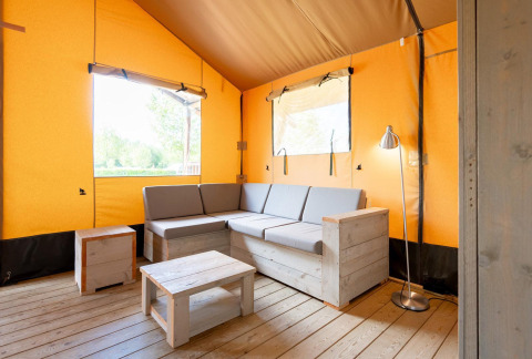 Zona giorno all'interno di una tenda safari Villatent Nomad con divano grigio, mobili in legno e pareti gialle.