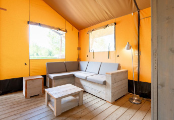 Innenraum des Villatent Nomad Safarizelts mit Holzmöbeln, grauem Sofa und heller Atmosphäre.